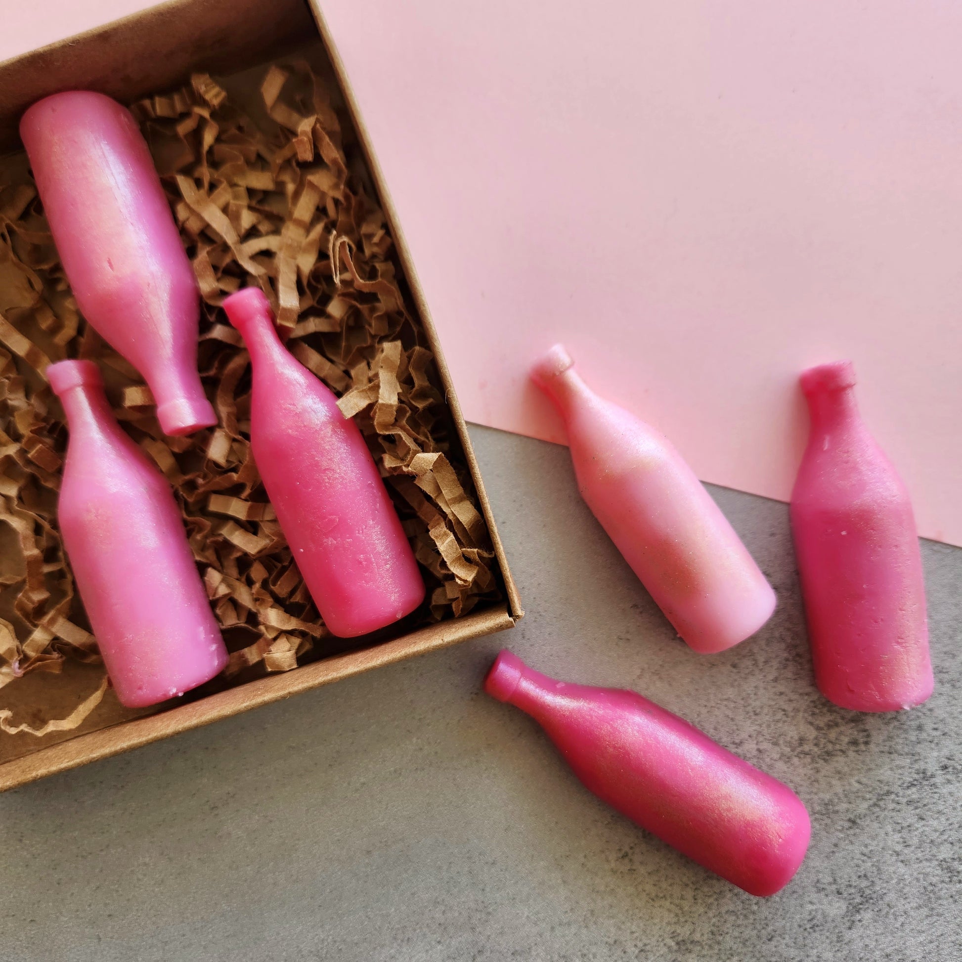 Close-up of pink wine bottle-shaped wax melts with a "Strawberry Wine" scent, arranged in a box with brown paper filler