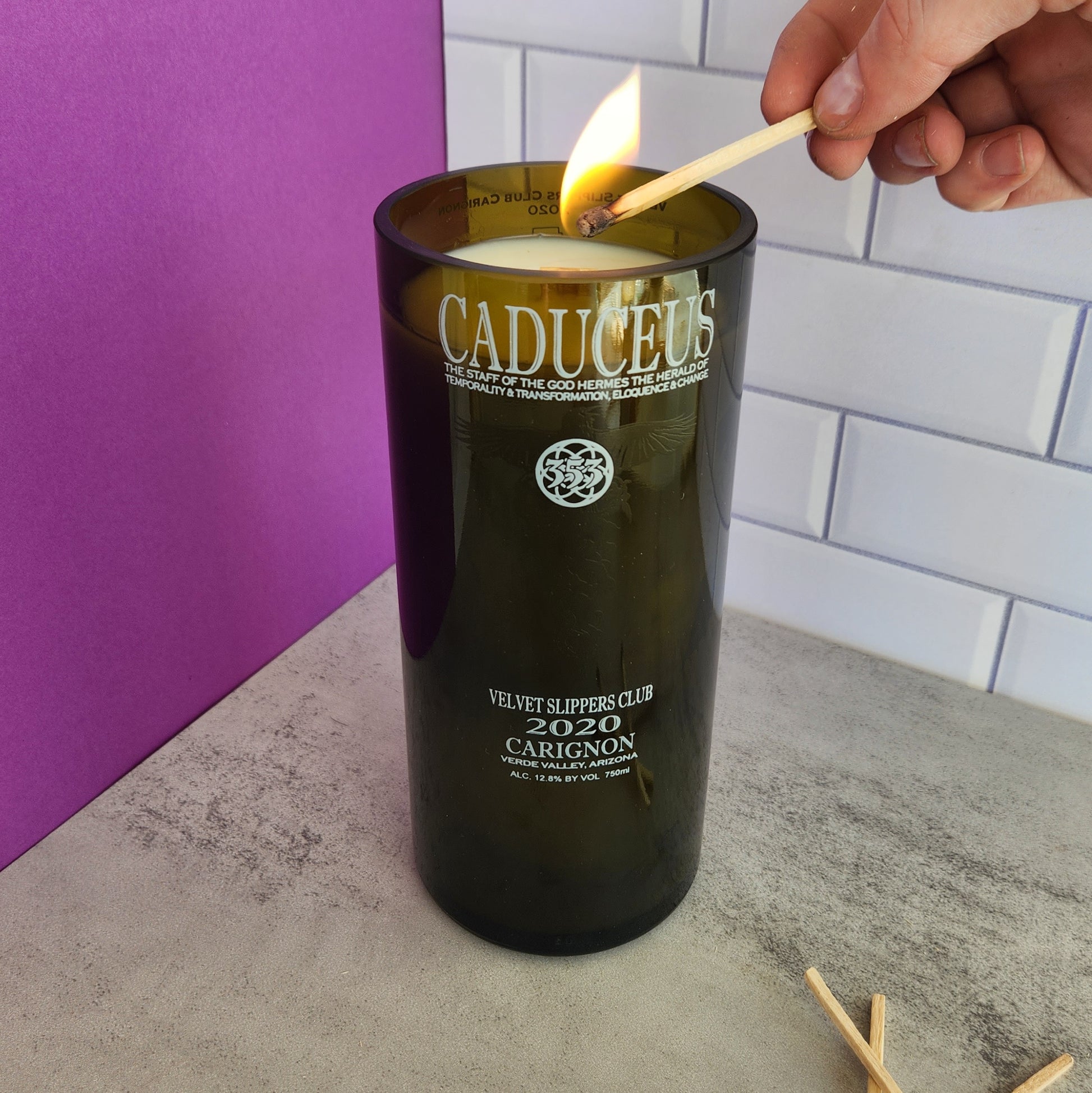 Close-up action shot of lighting the "Vanilla Twist" scented candle, capturing the glow of the flame and the recycled wine bottle design.