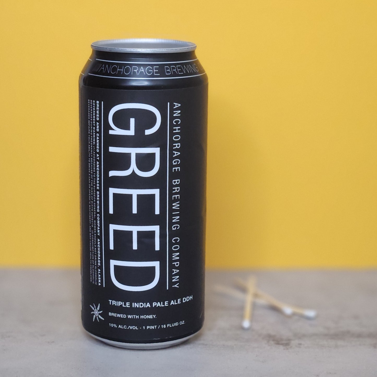 Full view of the recycled beer can candle labeled 'Greed' by Anchorage Brewing Company, highlighting its recycled nature and stylish design as part of the Cactus+Vine collection