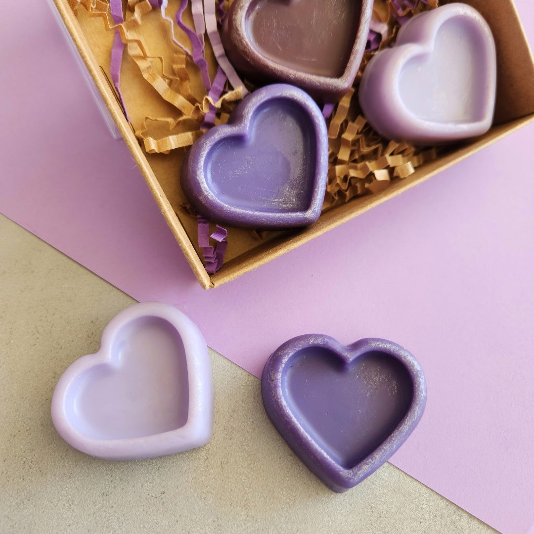 Close-up of heart-shaped Lavender Library wax melts in shades of purple, displayed on a pastel purple background with eco-friendly packaging.