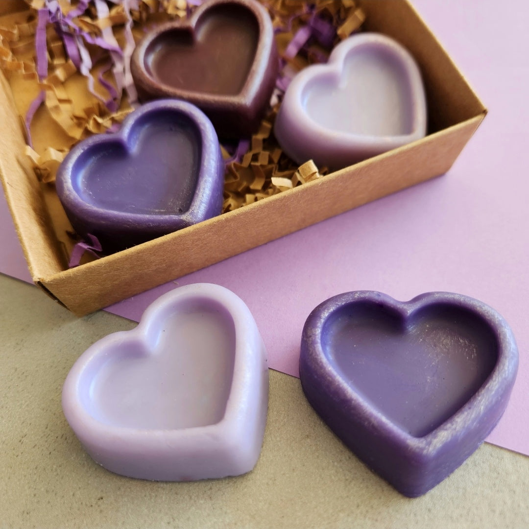 Heart-shaped Lavender Library wax melts in purple shades arranged on a table with some placed outside the box, set against a purple-themed background.