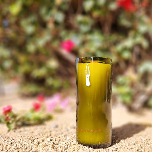 Showcasing a vibrant hand-poured candle in a recycled Arizona wine bottle, this piece brings eco-luxury to life. Captured in a sunlit desert setting with blooming flowers, it highlights sustainability and beauty.