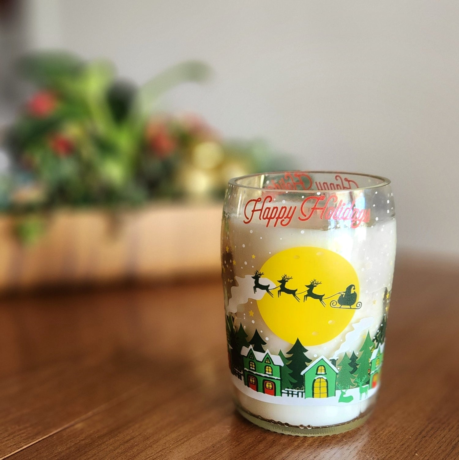 This festive candle, set in a recycled prosecco bottle featuring a charming holiday village and Santa's sleigh, radiates warmth and seasonal magic