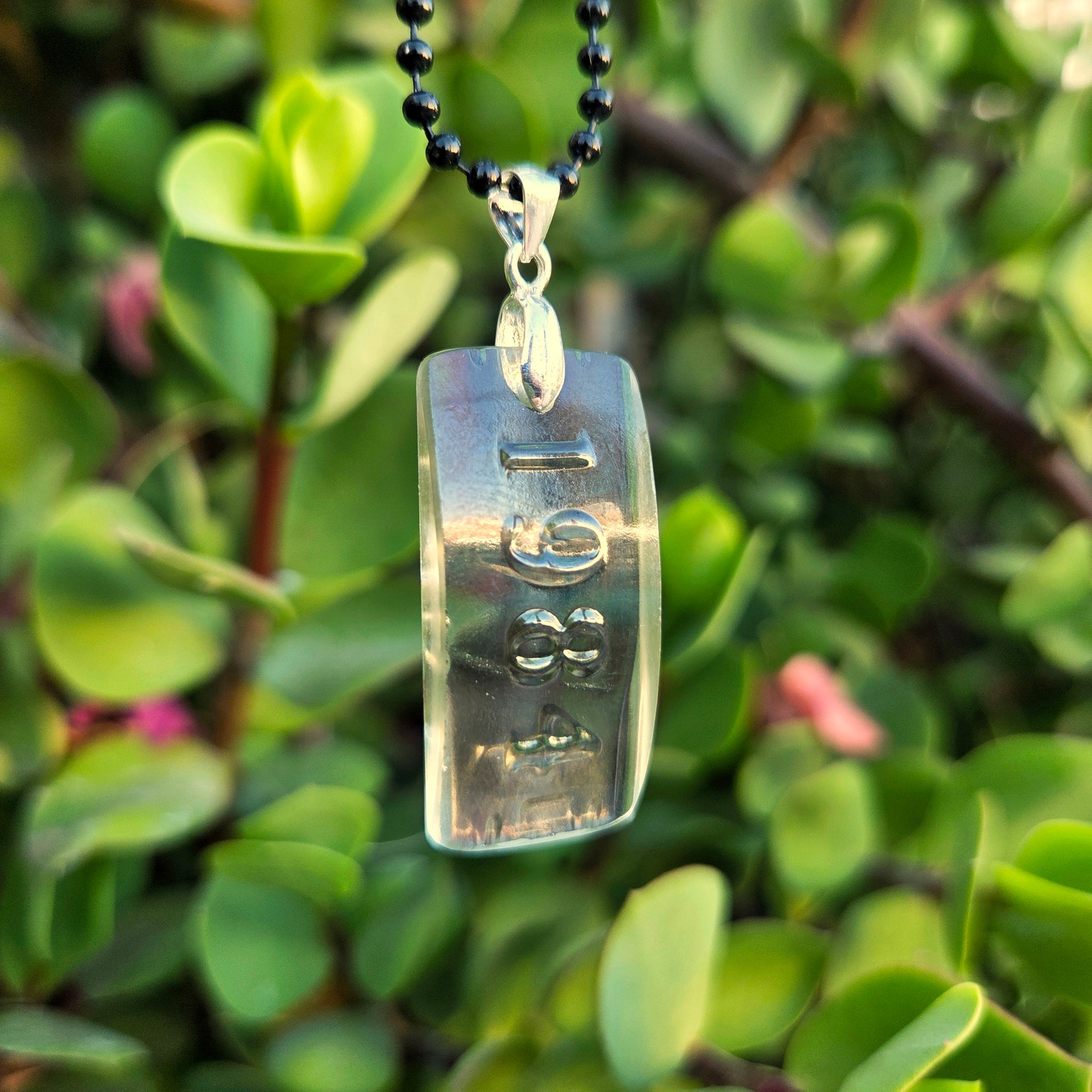 A clear glass pendant with raised numbers saying 1984 hanging in front of lush greenery.