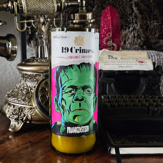 Front-facing 19 Crimes Frankenstein wine bottle candle featuring vivid green and magenta artwork of Frankenstein’s monster, hand-poured with coconut soy wax and a wooden wick in a recycled bottle.