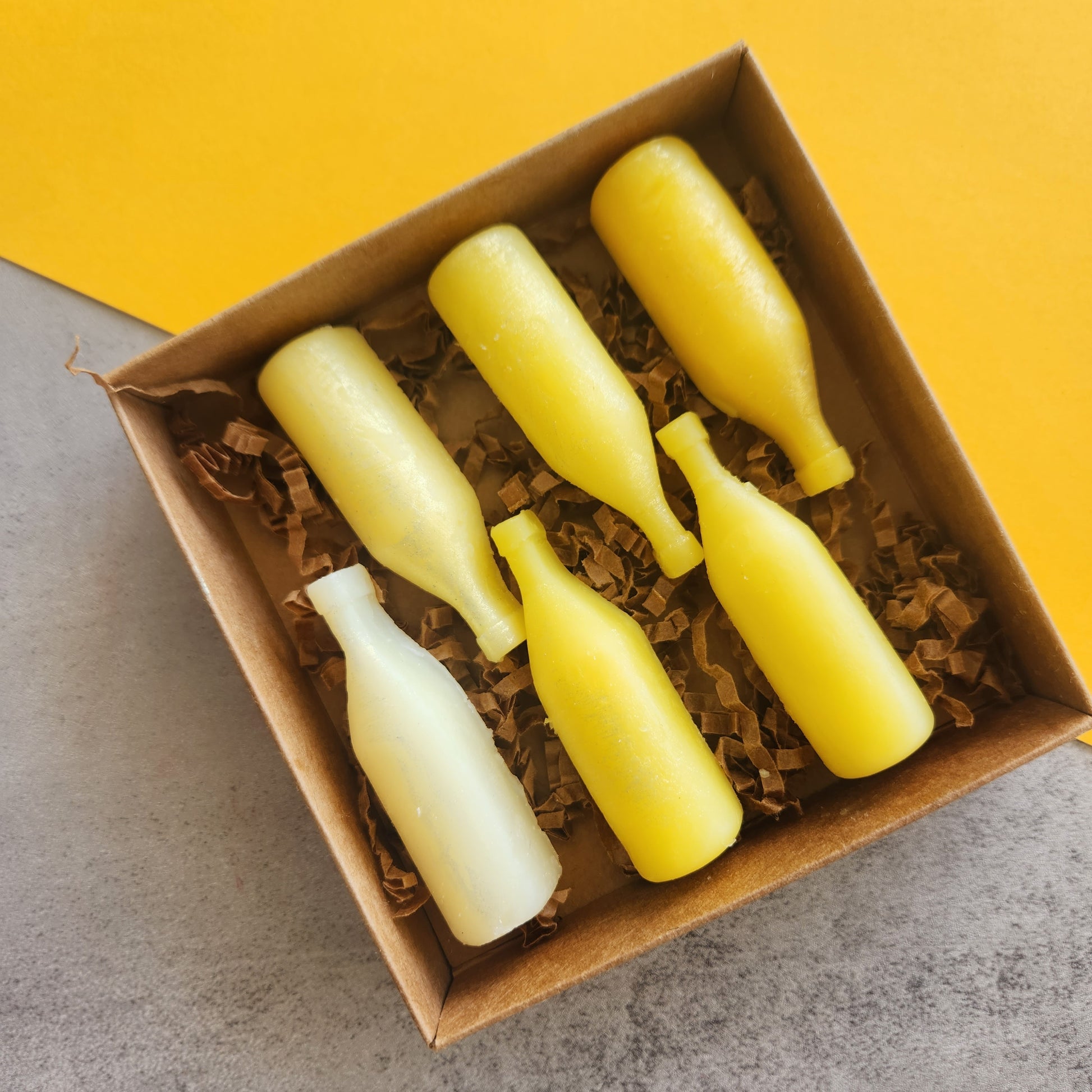 Top-down view of six yellow wine bottle-shaped wax melts in a box on a yellow background