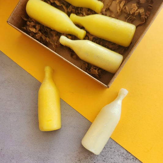 6 small yellow bottle shaped wax melts are displayed artfully.