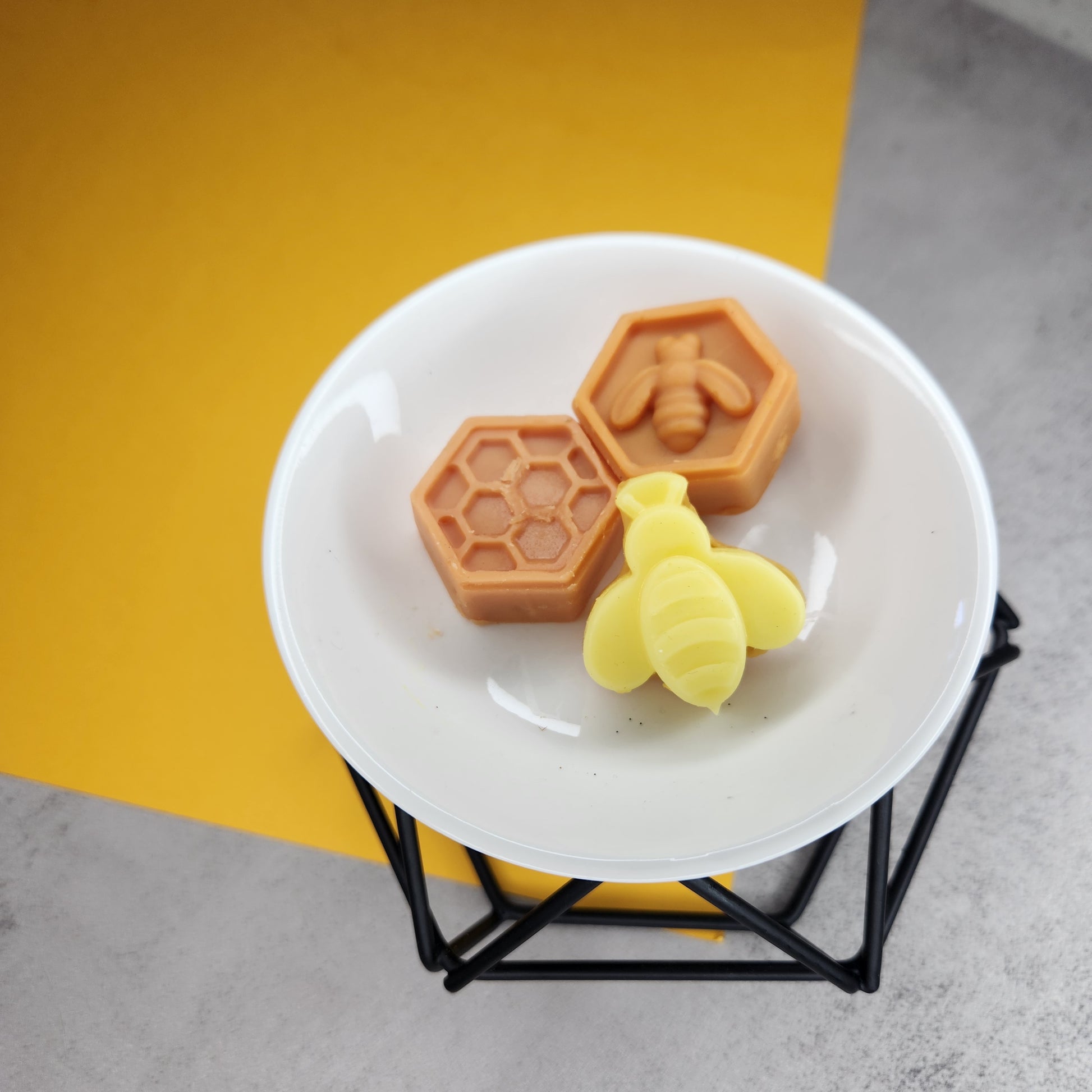 Three Goldwater Spiced Honey Vanilla wax melts shaped like a bee and honeycombs, arranged on a white wax melter with a yellow background