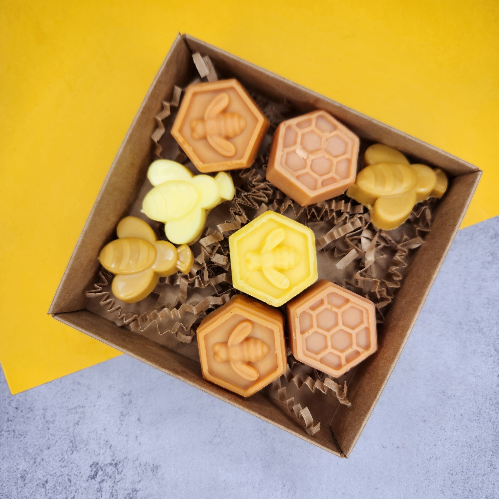 Top-down view of a box of Goldwater wax melts in various shades of yellow and honey, showcasing bee and honeycomb designs