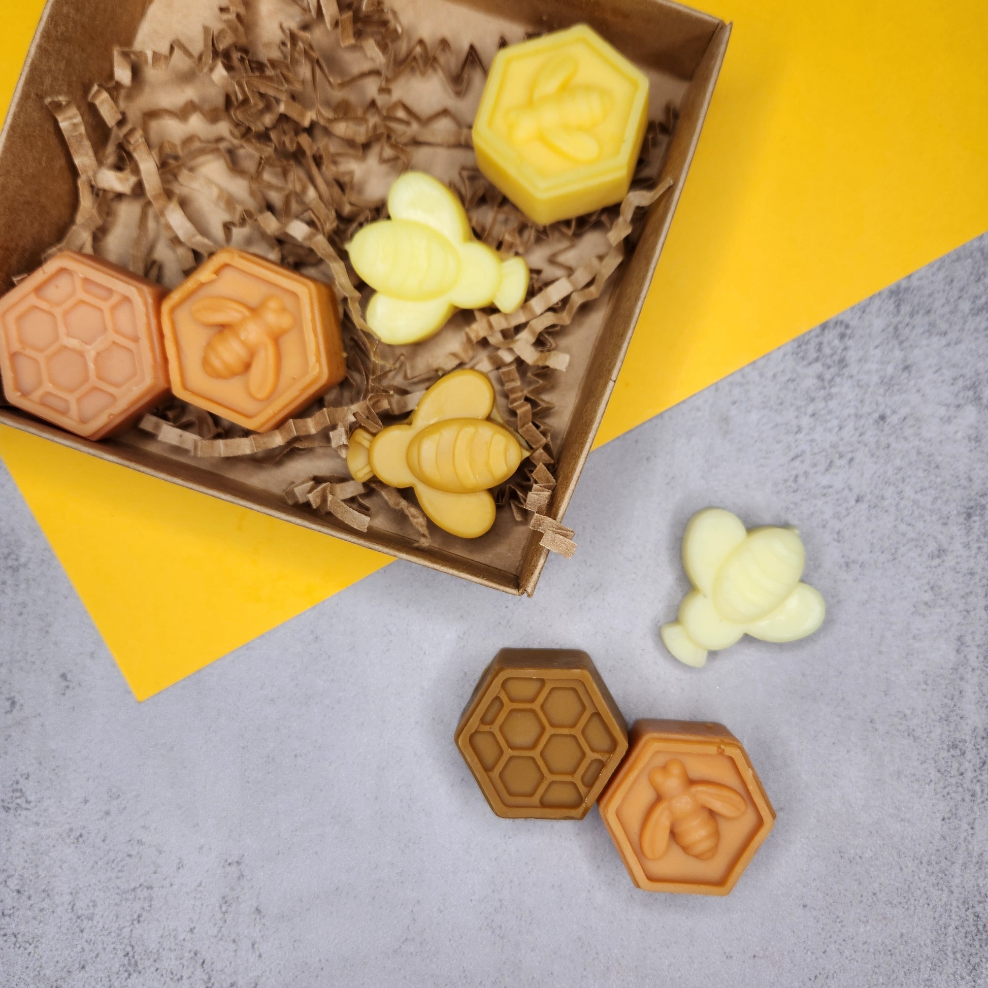 An overhead shot of Goldwater Spiced Honey Vanilla wax melts in bee and honeycomb shapes, neatly arranged in a kraft box with shredded paper.