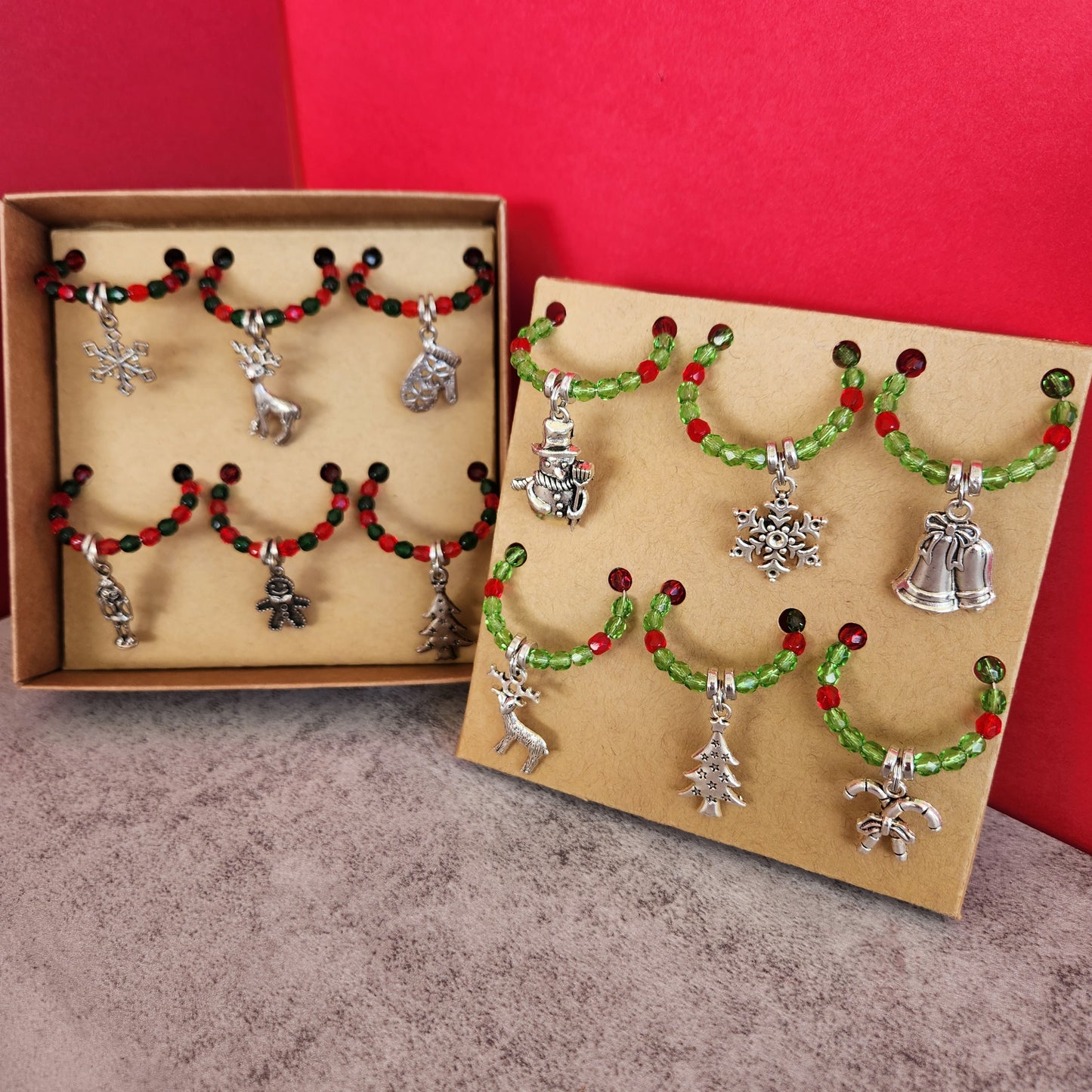 Two Sets of Festive Wine Glass Charms Displayed in Gift Boxes, Showing Various Christmas Charms like Snowflakes and Bells, Ideal for Holiday Gatherings