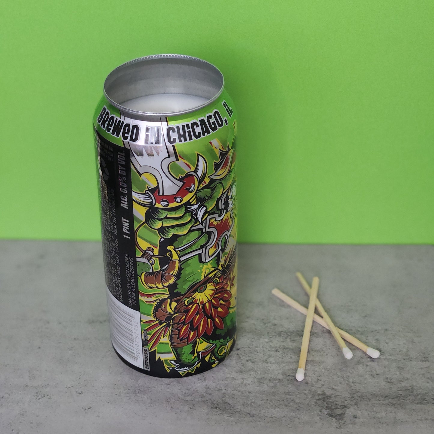 Side view of a Bourbon Lime scented candle in a recycled Lizard King beer can, showcasing the intricate artwork and bright colors against a fresh green background, ideal for sustainable home decor lovers.