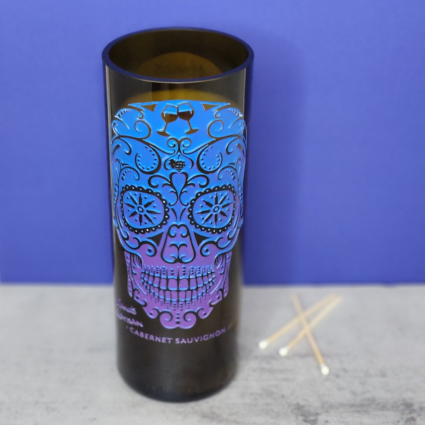 Front view of the Autumn Campfire candle in a recycled wine bottle featuring a vibrant blue and purple sugar skull design with intricate patterns, highlighting its unique and artistic home decor appeal