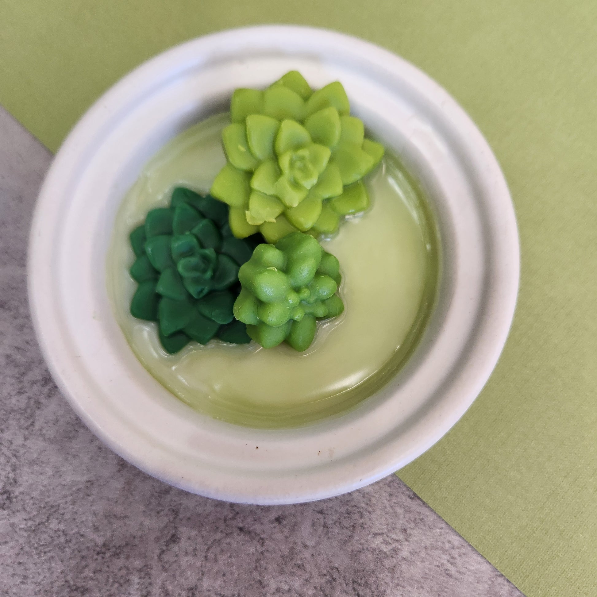 Close-up of eco-friendly soy wax melts shaped like succulents in shades of green, arranged in a wax melter, perfect for home fragrance and décor. Succulent-shaped wax melts for aromatherapy and decorative use.