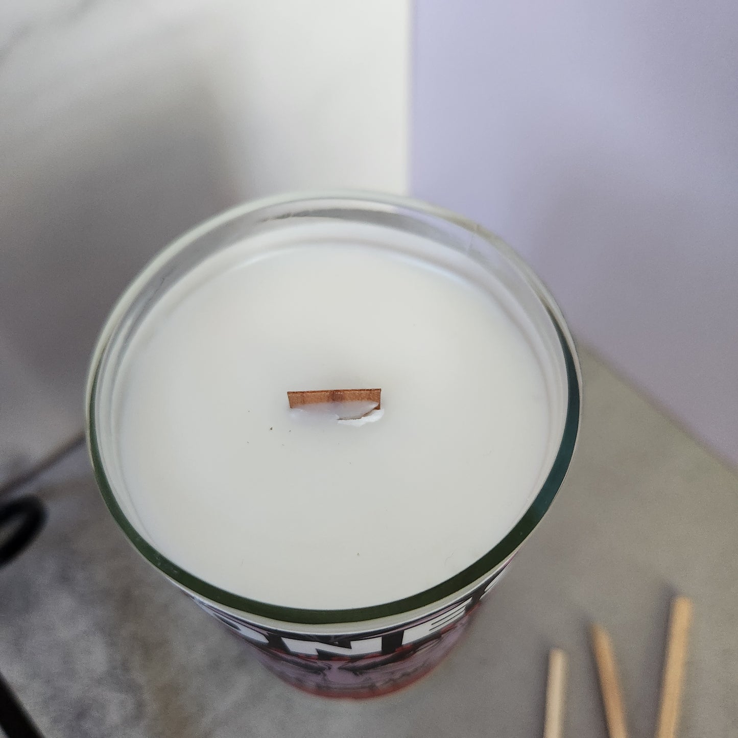 Top view of a coconut-soy wax candle with wooden wick, housed in a recycled Jones soda bottle with vampire label, ideal for sustainable Halloween decor.