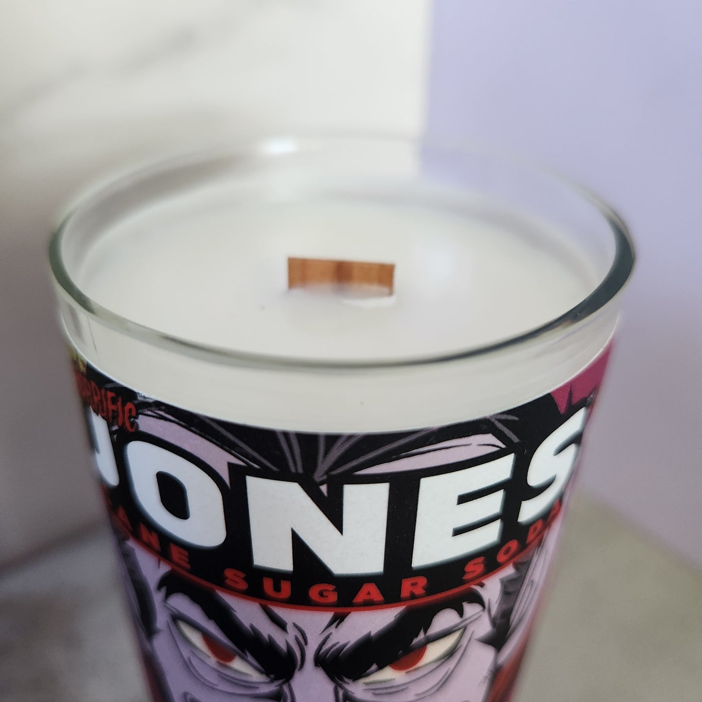 Close-up of a hand-poured coconut-soy wax candle in a recycled Jones soda bottle with a vampire graphic label, showcasing the wooden wick.