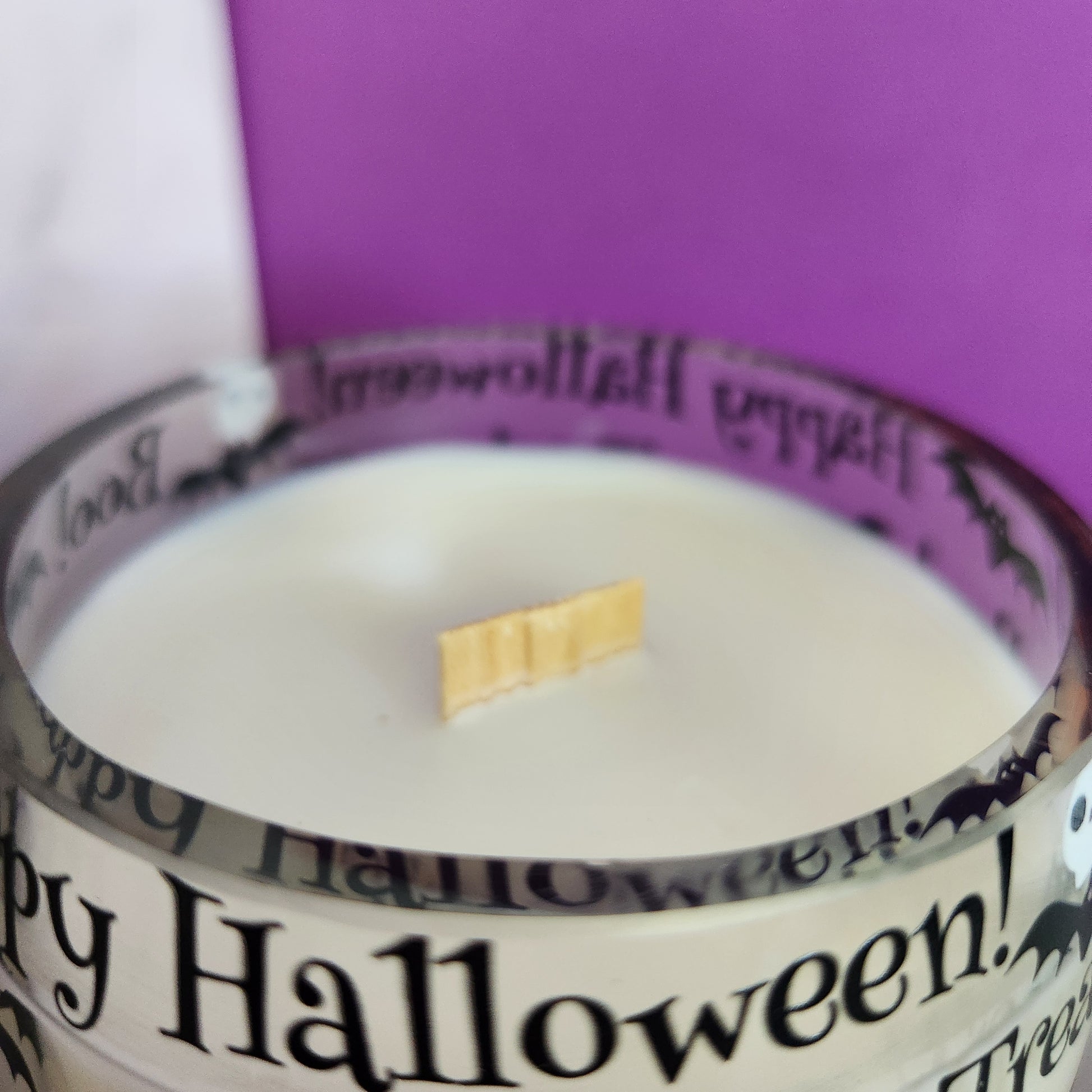 Close-up of the wooden wick and smooth glass rim in a Caramel Apple scented Halloween-themed wine bottle candle with jack-o'-lanterns, bats, and skulls, made with eco-friendly coconut soy wax.