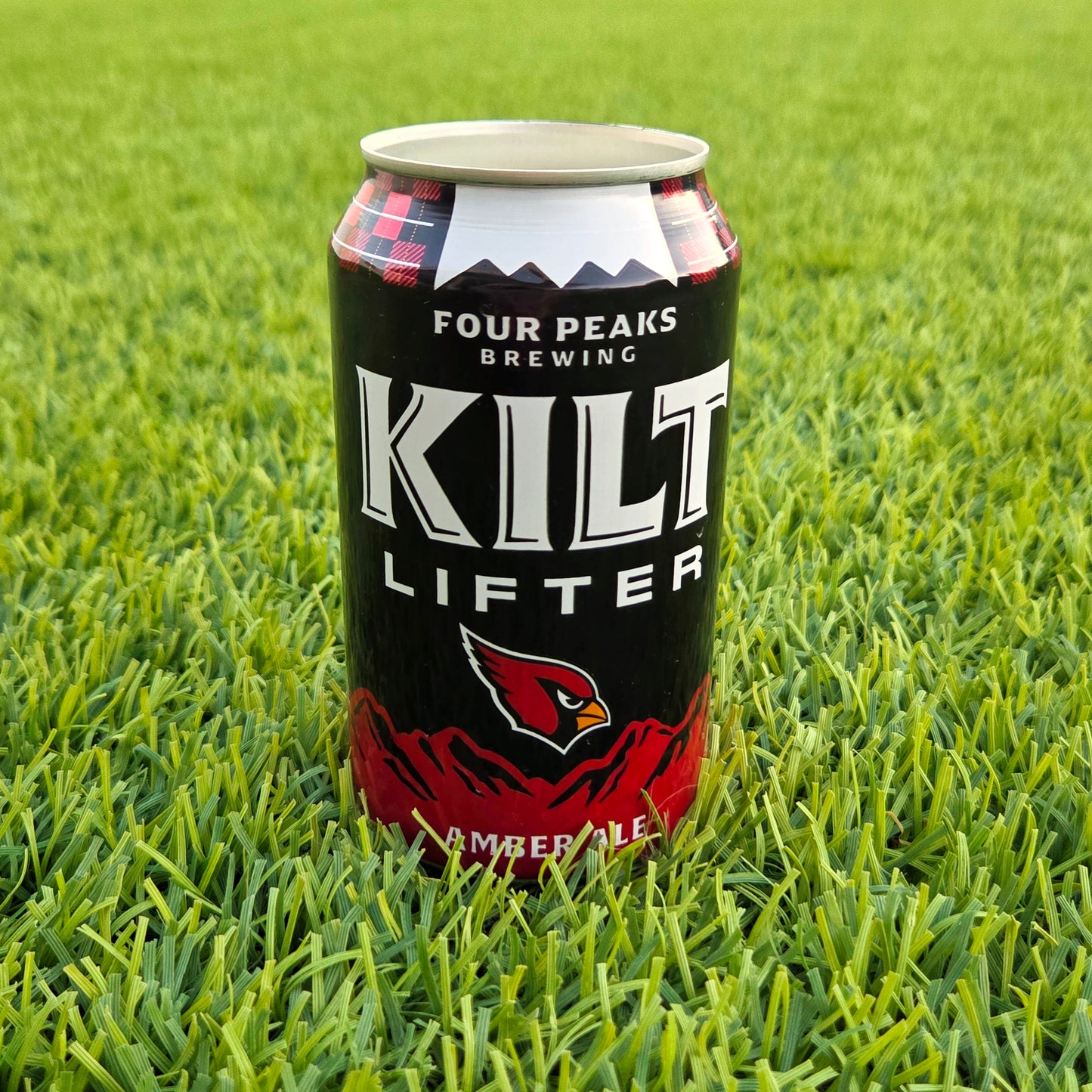 Recycled beer can with the AZ cardinals logo, made into a cande.  sitting on the grass.