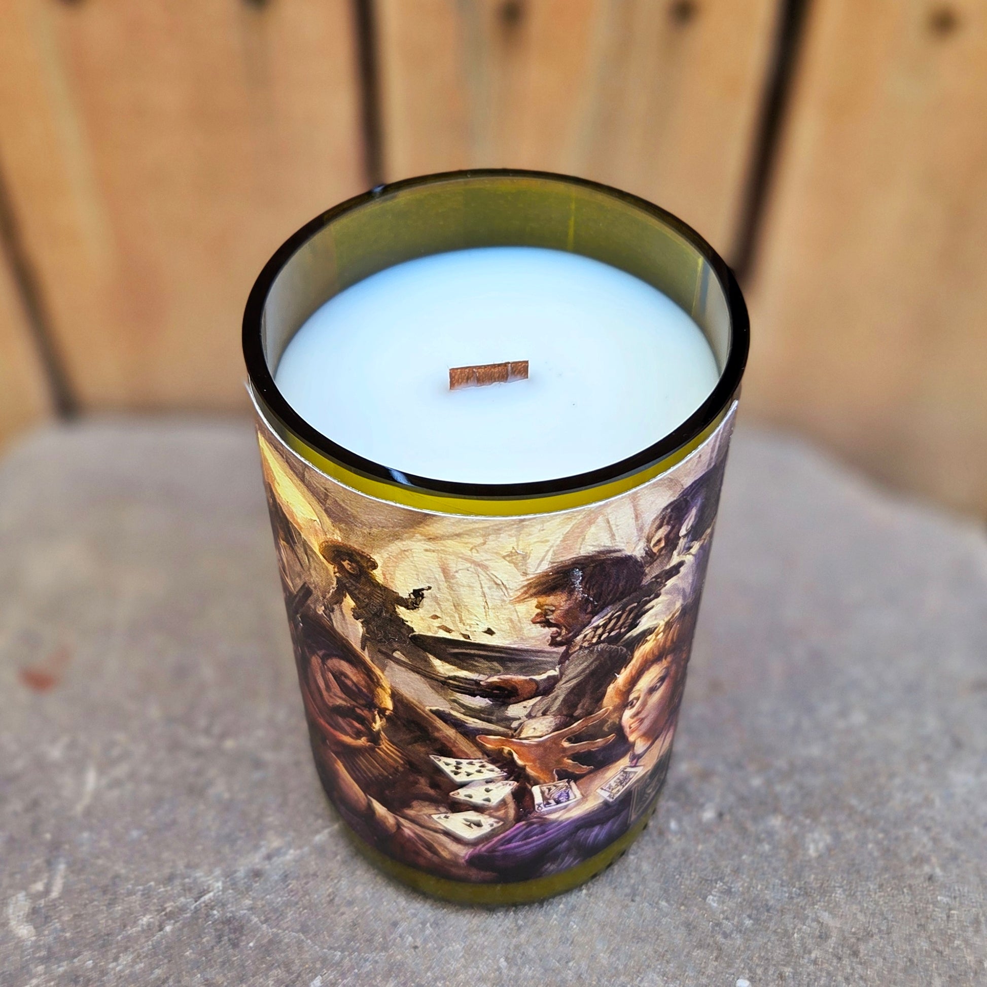 Angled shot of a recycled wine bottle candle featuring lively saloon shootout art with playing cards mid-air. This eco-friendly piece is filled with coconut soy wax and a wooden wick.