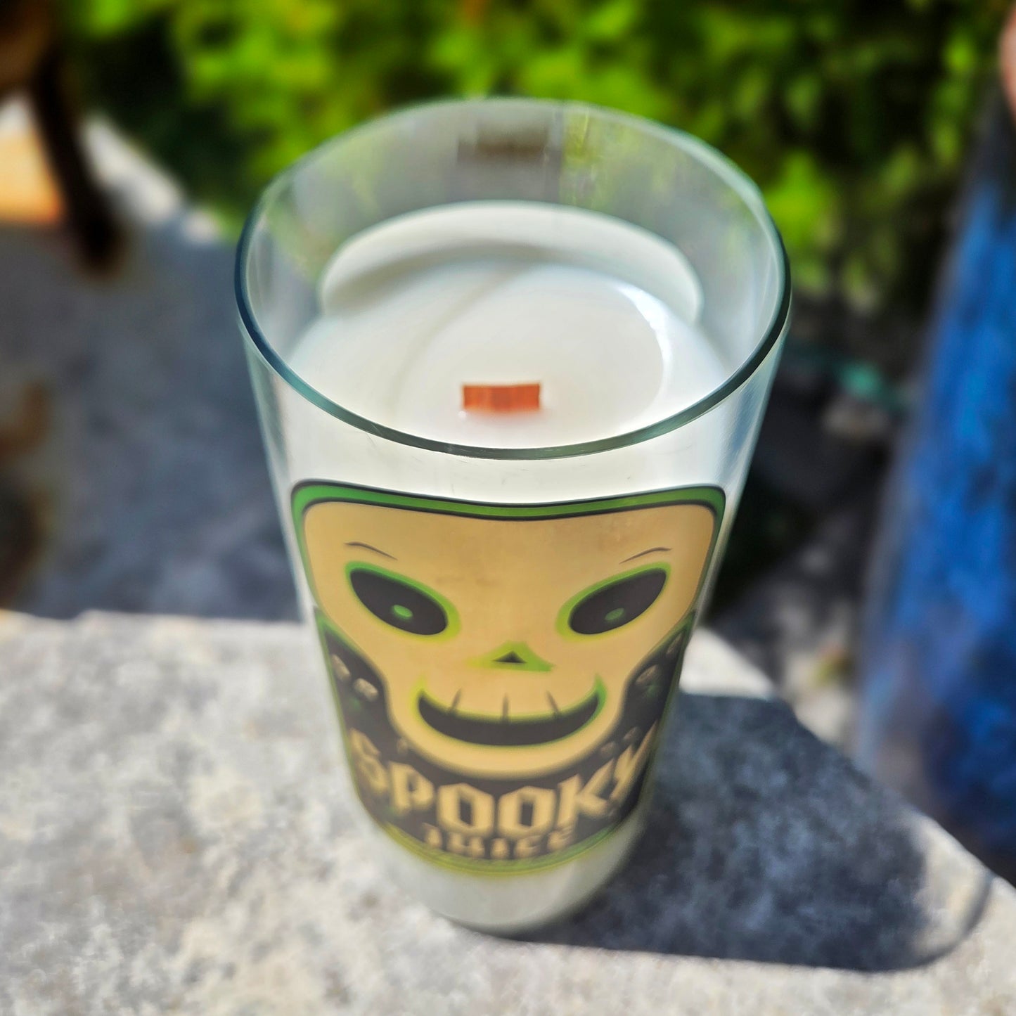 Angled shot of a Spooky Juice wine bottle candle with a bold skull design label in green and black. Hand-poured coconut soy wax and a wooden wick make this eco-friendly candle both spooky and sustainable.