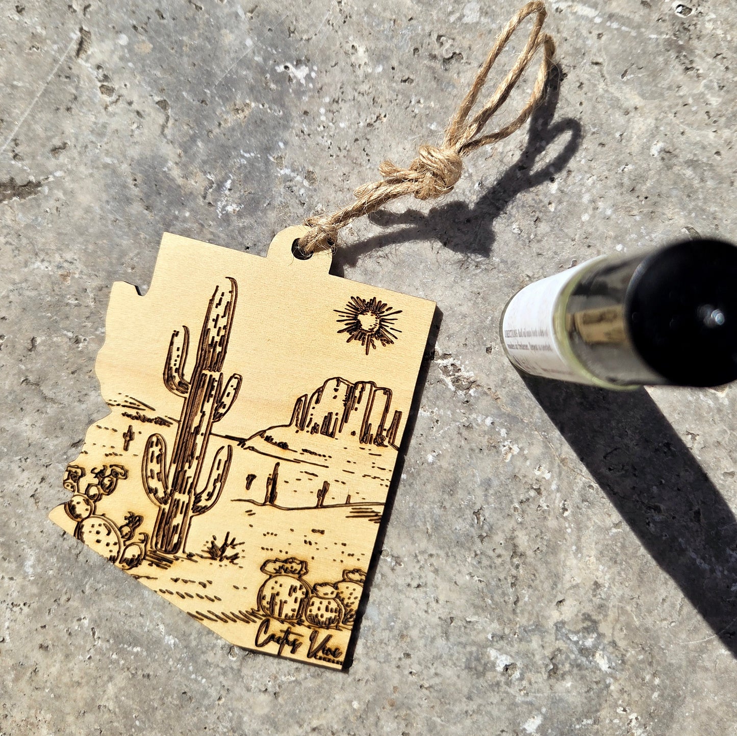 Arizona wood hanger with desert scene and cactus design on a concrete surface with a bottle.