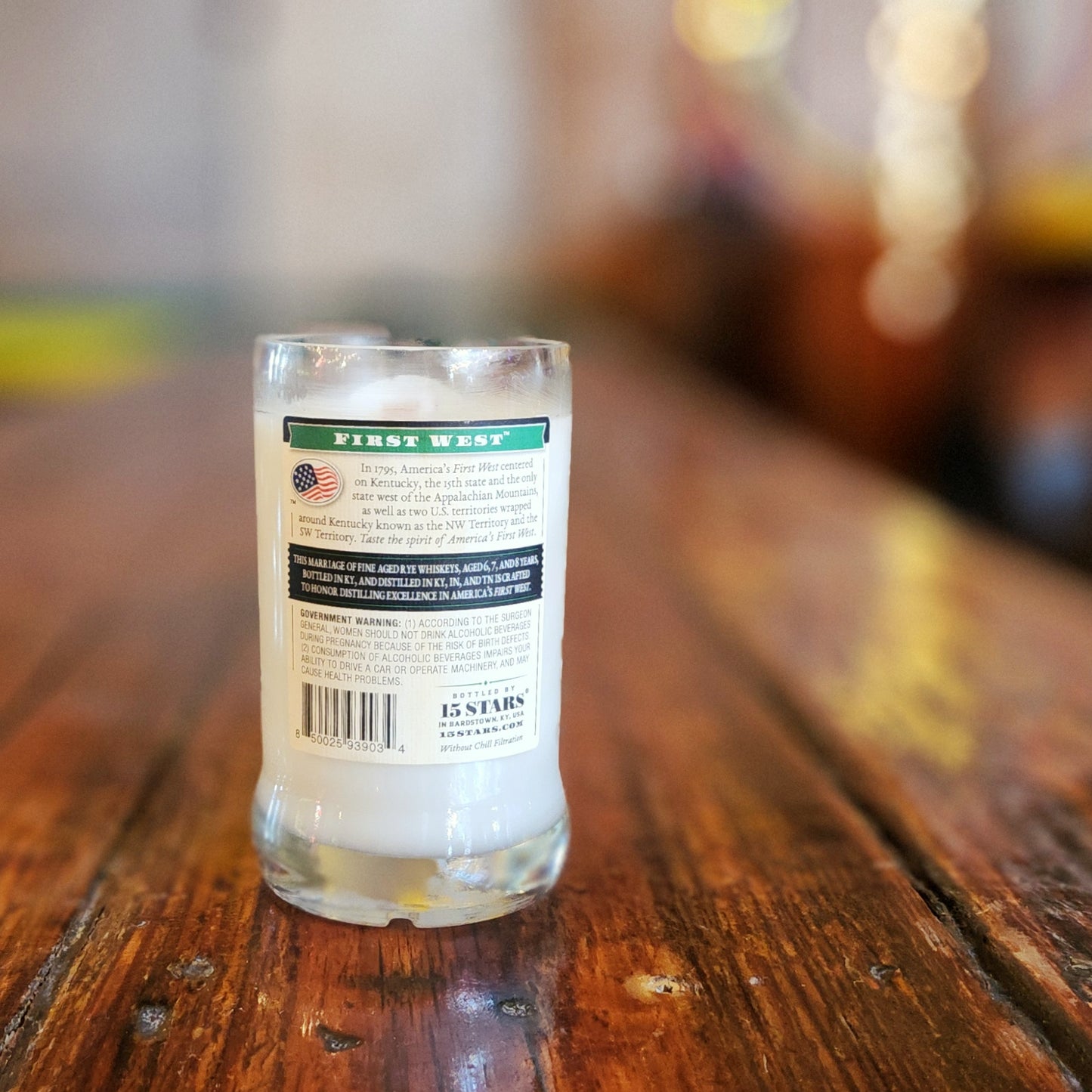 Eco-friendly liquor bottle candle made from a 15 Stars Fine Aged Rye bottle, showcasing the back label against a rustic wooden table.