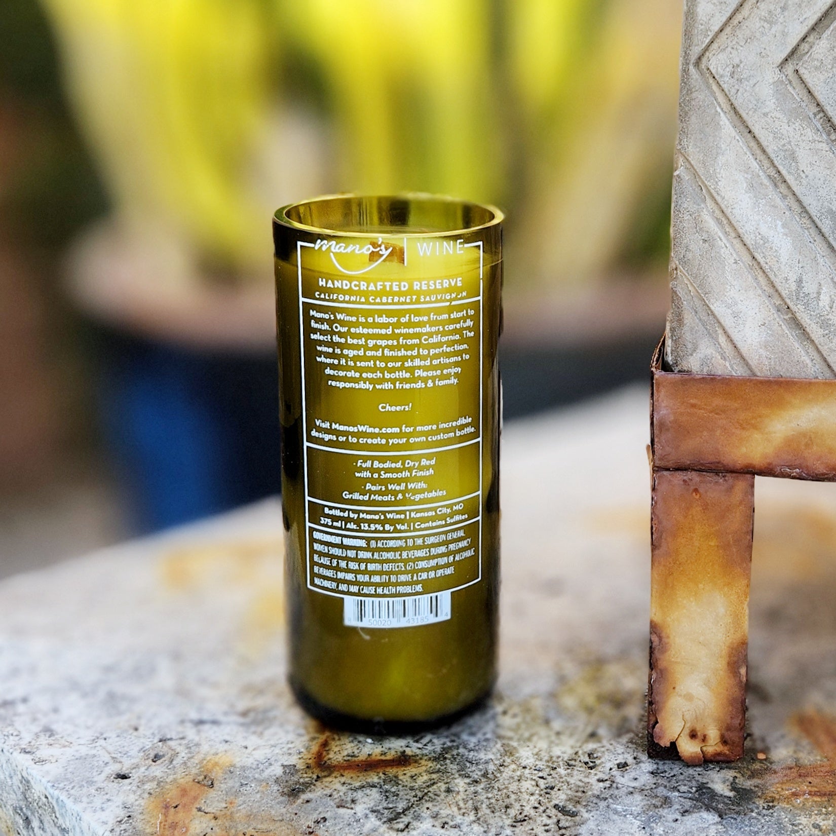 Back label view of a recycled green wine bottle candle, repurposed from a Mamos wine bottle. The label details the handcrafted reserve’s origin, adding authenticity to this clean-burning, coconut soy wax candle.

