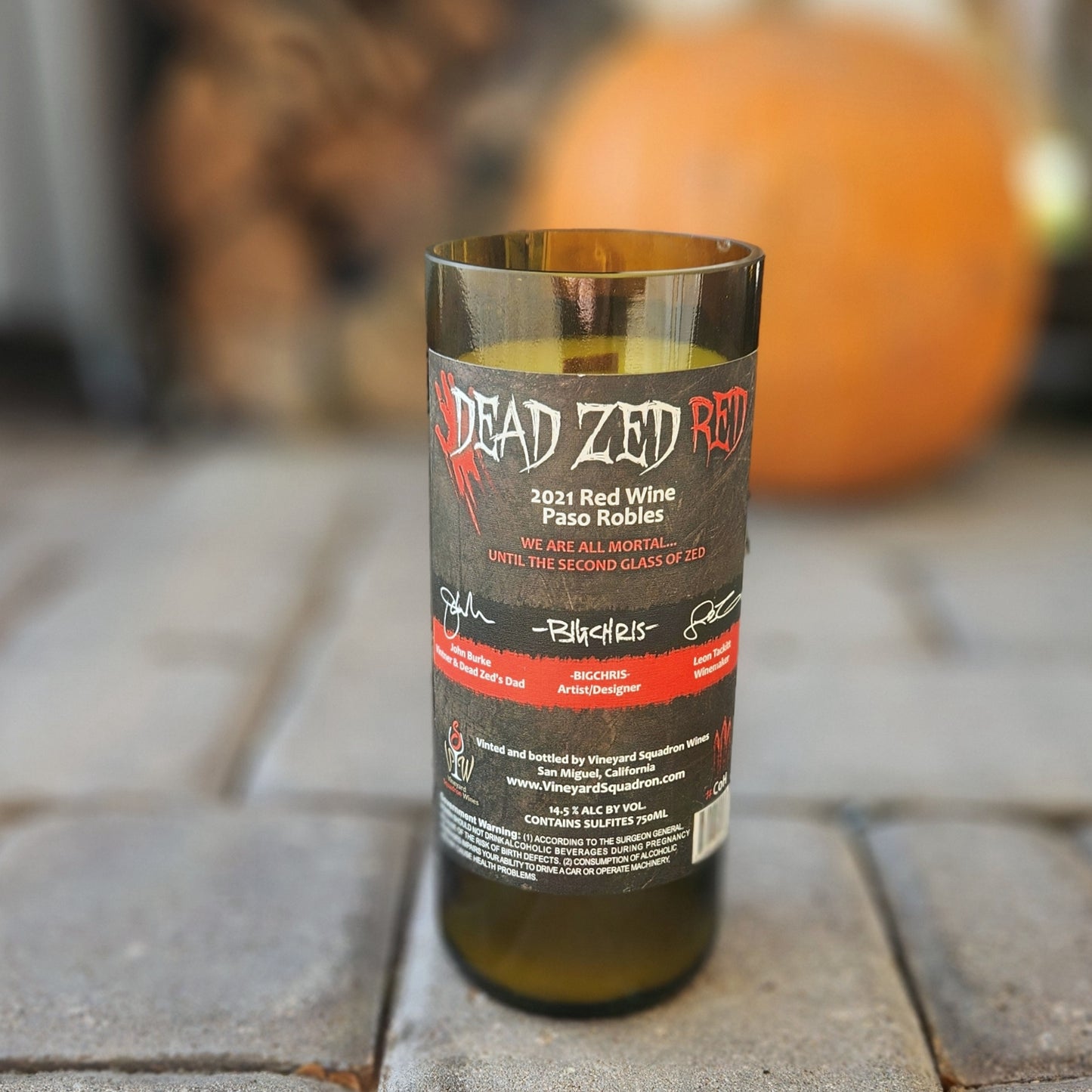 Back label of a Dead Zed Red recycled wine bottle candle, showing the label’s quirky slogan and signatures. The candle is hand-poured with non-toxic wax and features a wooden wick inside.