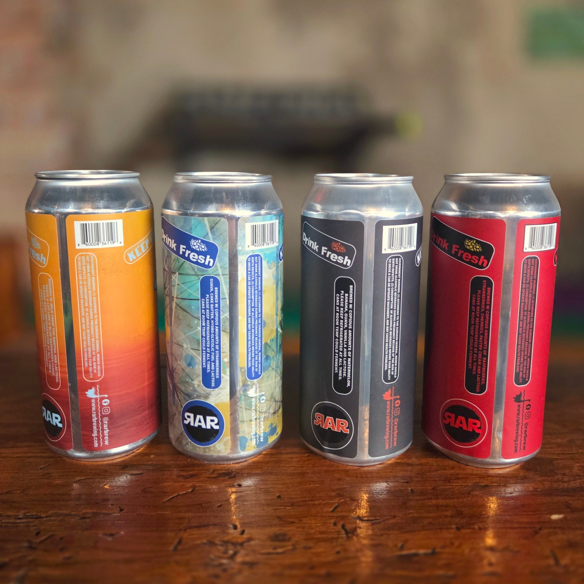 Rear view of four upcycled RaR Brewing beer can candles showing barcode labels and "Drink Fresh" text, highlighting their origin before being repurposed into eco-friendly candles with wooden wicks.