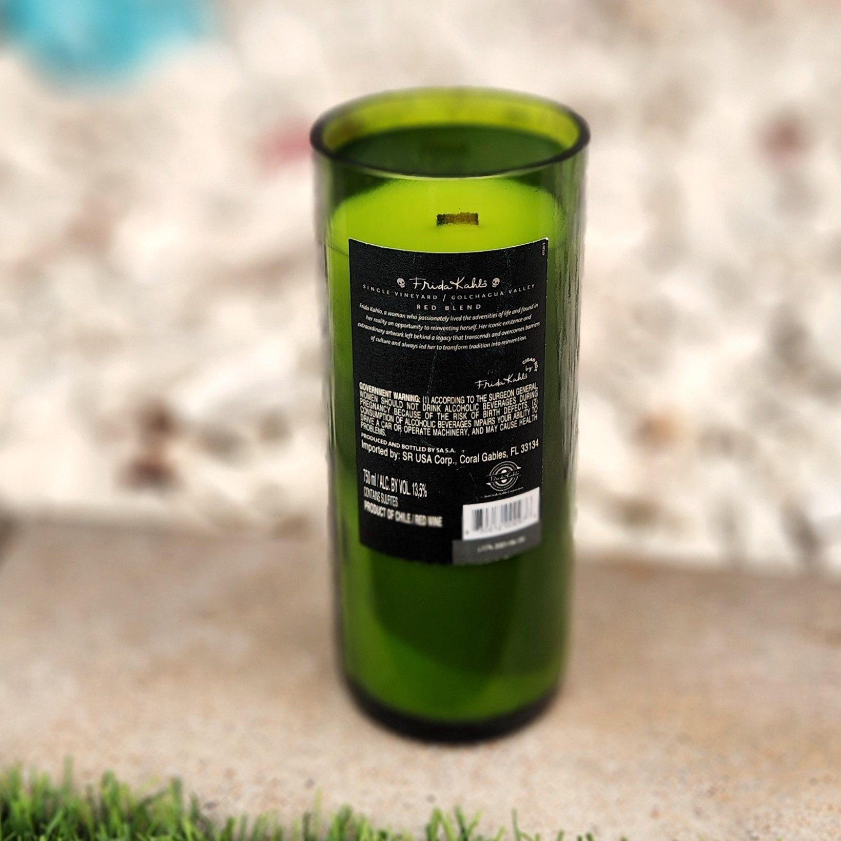 Eco-friendly wine bottle candle featuring a black Frida Kahlo label with vineyard and product info, hand-poured into a green recycled glass vessel with a smooth, shiny rim and clean-burning coconut soy wax inside.