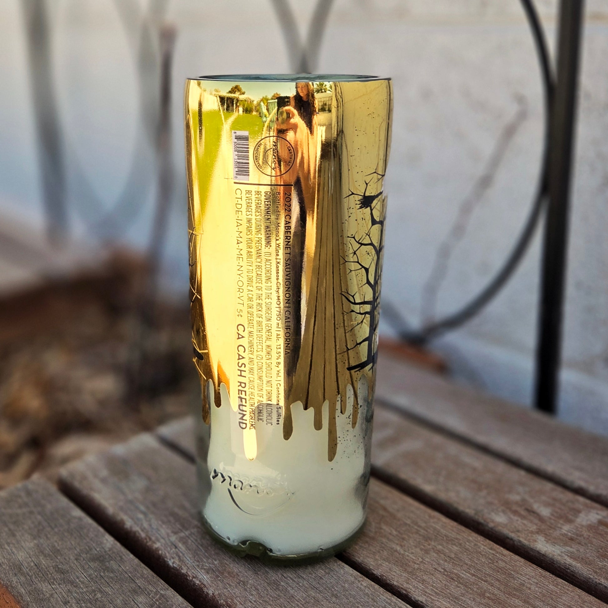 Recycled wine bottle candle with a reflective gold finish and printed label details. The eco-friendly design is hand-poured with coconut soy wax and a wooden wick for a clean, long-lasting burn.