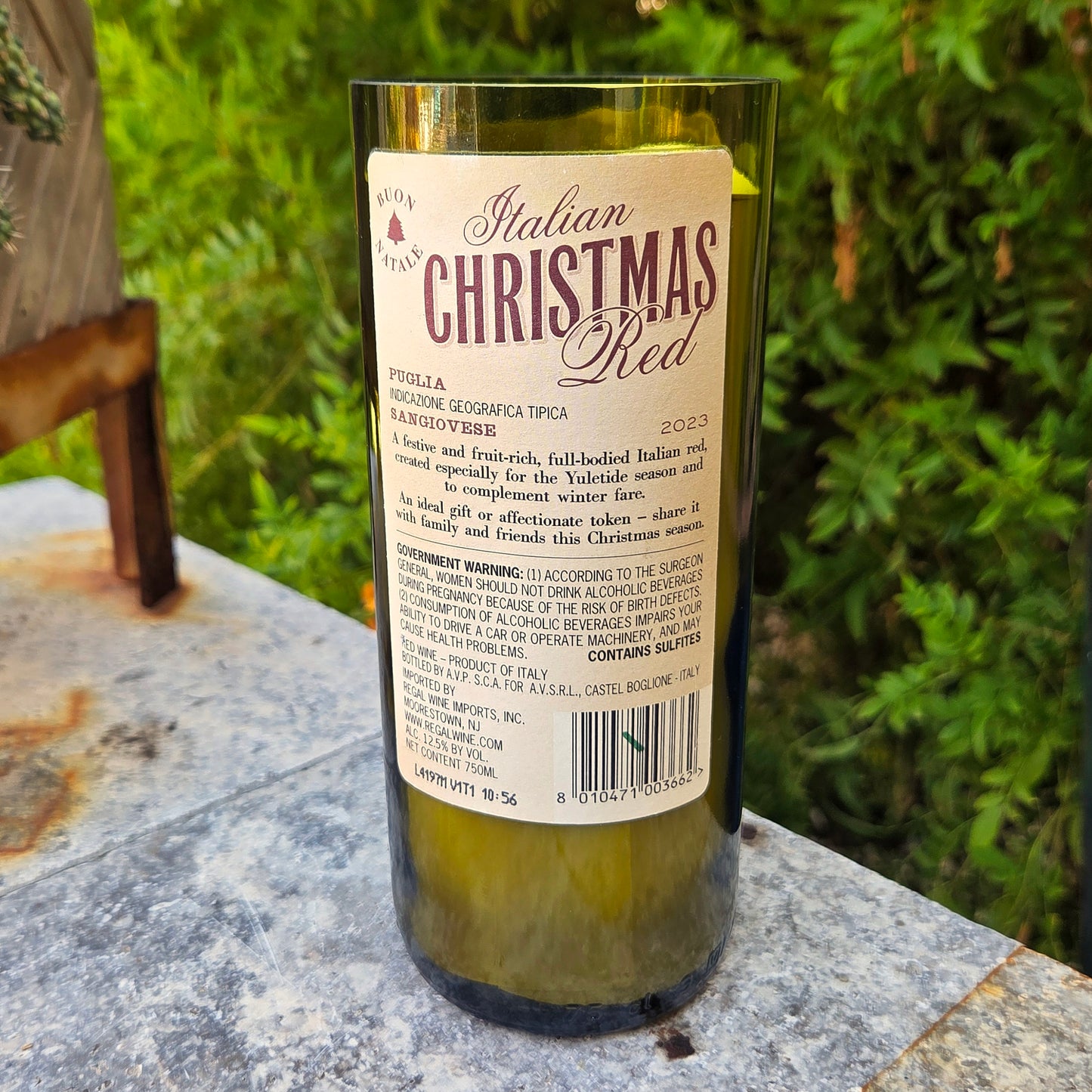 Wine bottle candle labeled 'Italian Christmas Red' on a stone surface with greenery in the background
