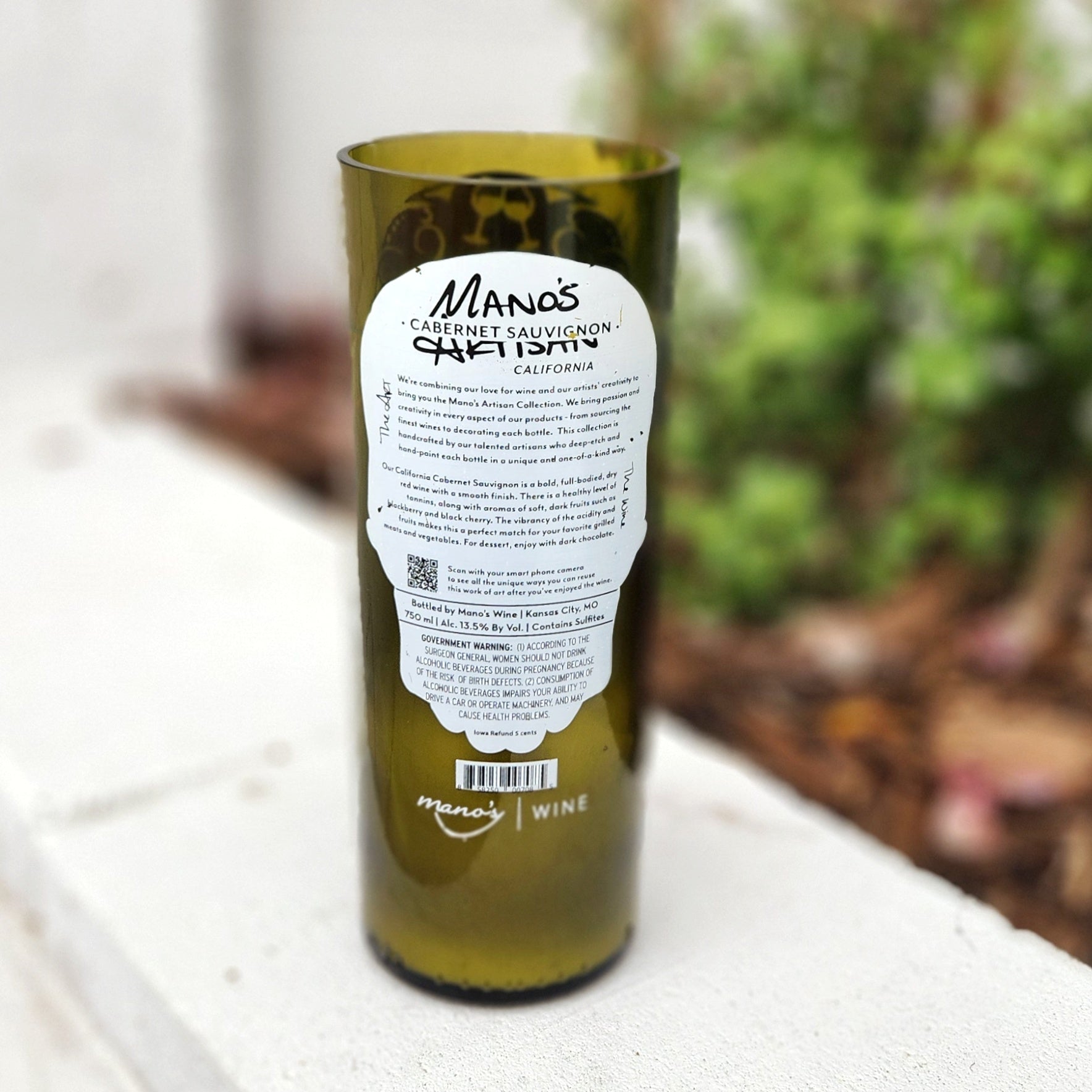 Back label of a clean-burning wine bottle candle in a recycled wine bottle, showcasing the original Manos Wine label. The bottle’s smooth glass rim and bold green tint highlight the sustainable craftsmanship behind this non-toxic, coconut soy wax candle.

