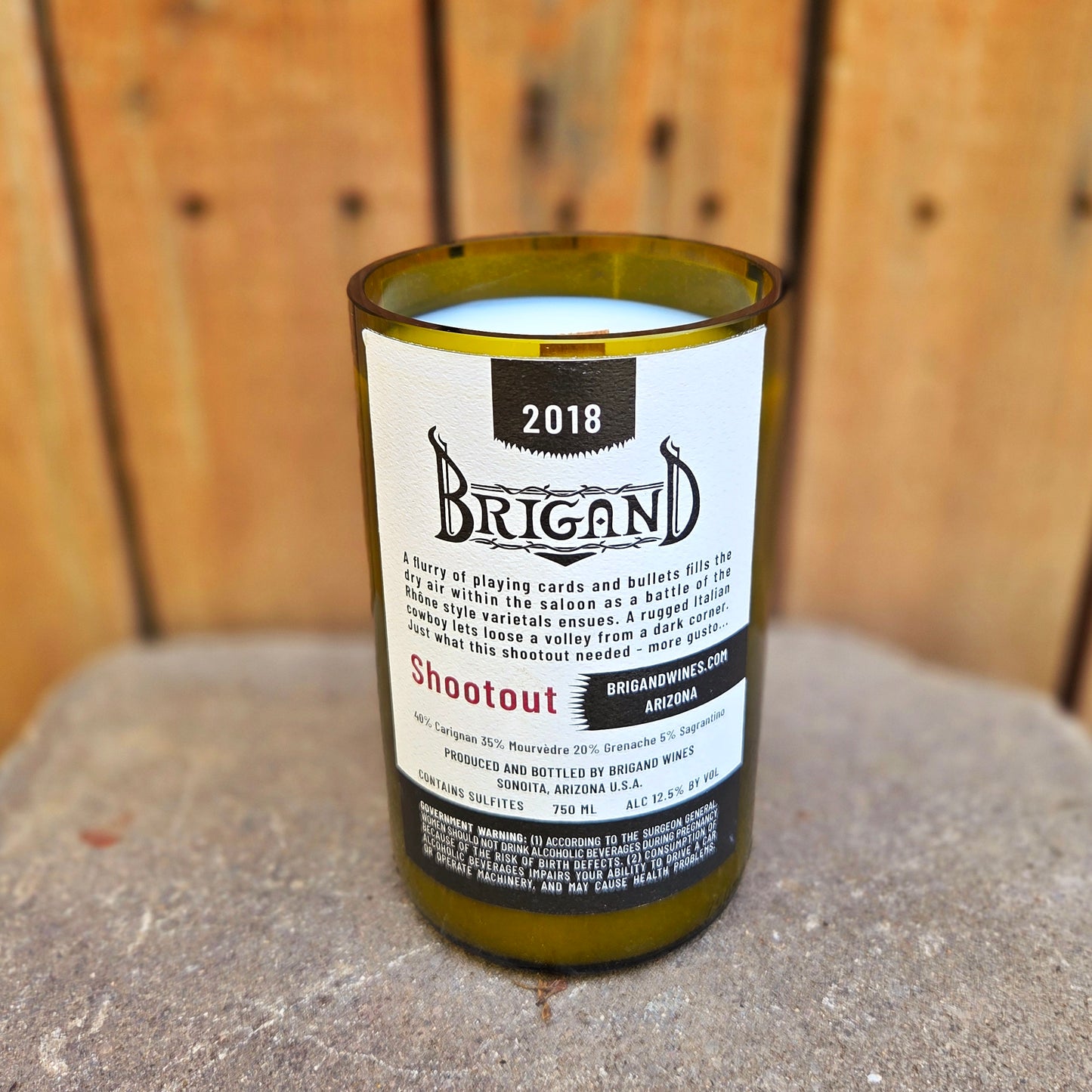 Eco-friendly wine bottle candle made from a recycled green glass bottle, featuring the Brigand “Shootout” wine label with detailed story text. Hand-poured with coconut soy wax and a wooden wick for a clean burn.