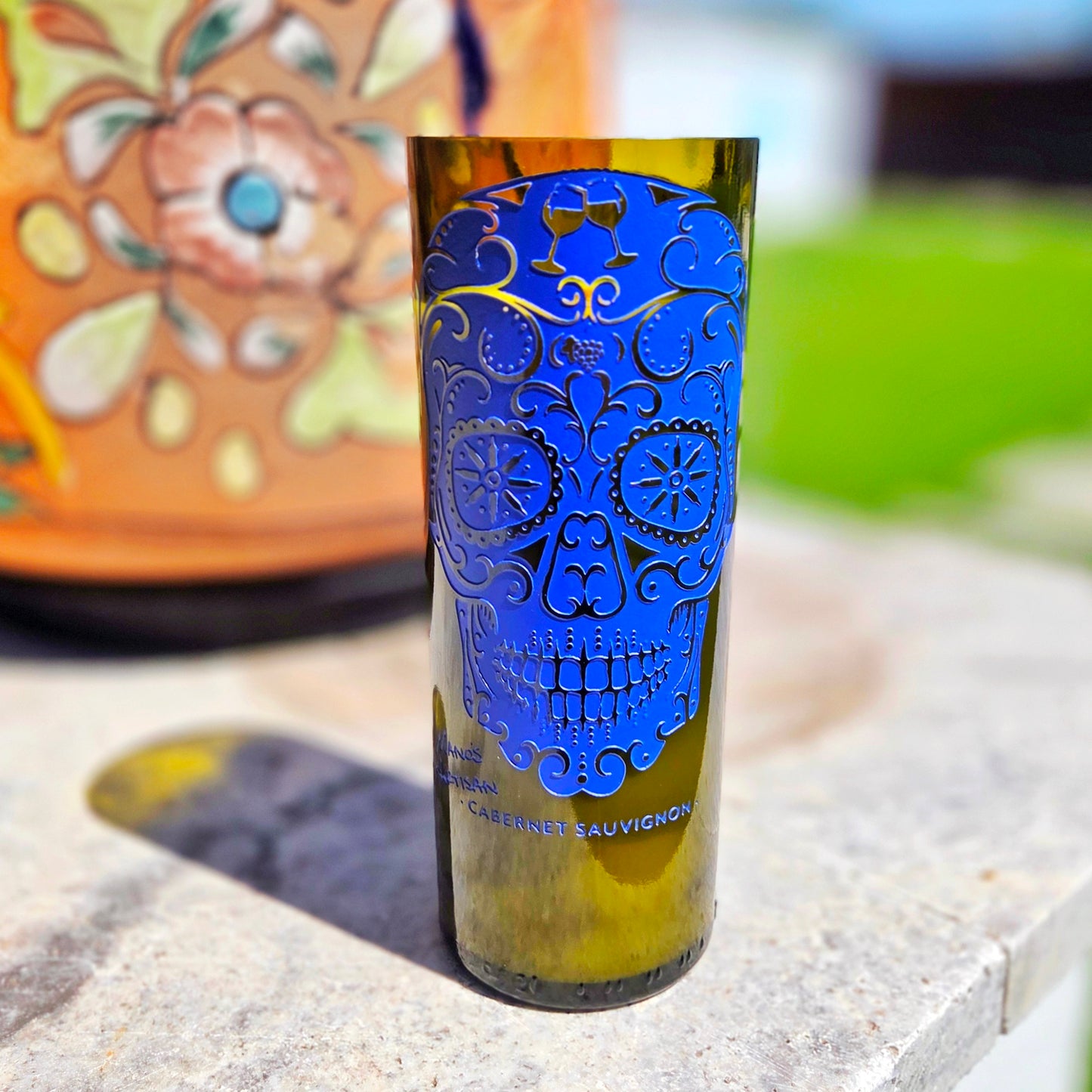 Front-facing view of a striking blue sugar skull wine bottle candle, crafted from a recycled Cabernet Sauvignon bottle and filled with clean-burning coconut soy wax and a wooden wick.