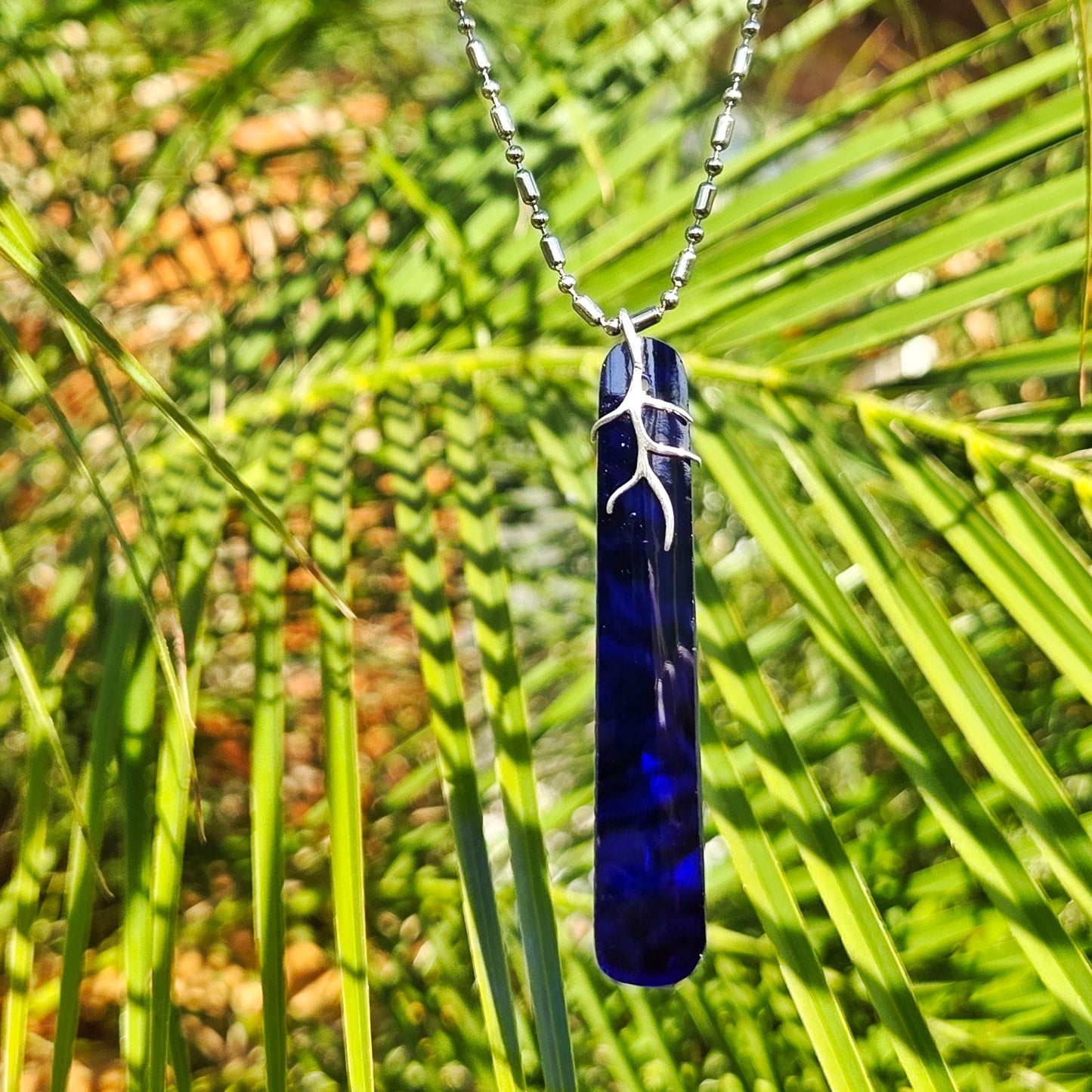 Blue glass pendant necklace with silver chain against a green leafy background