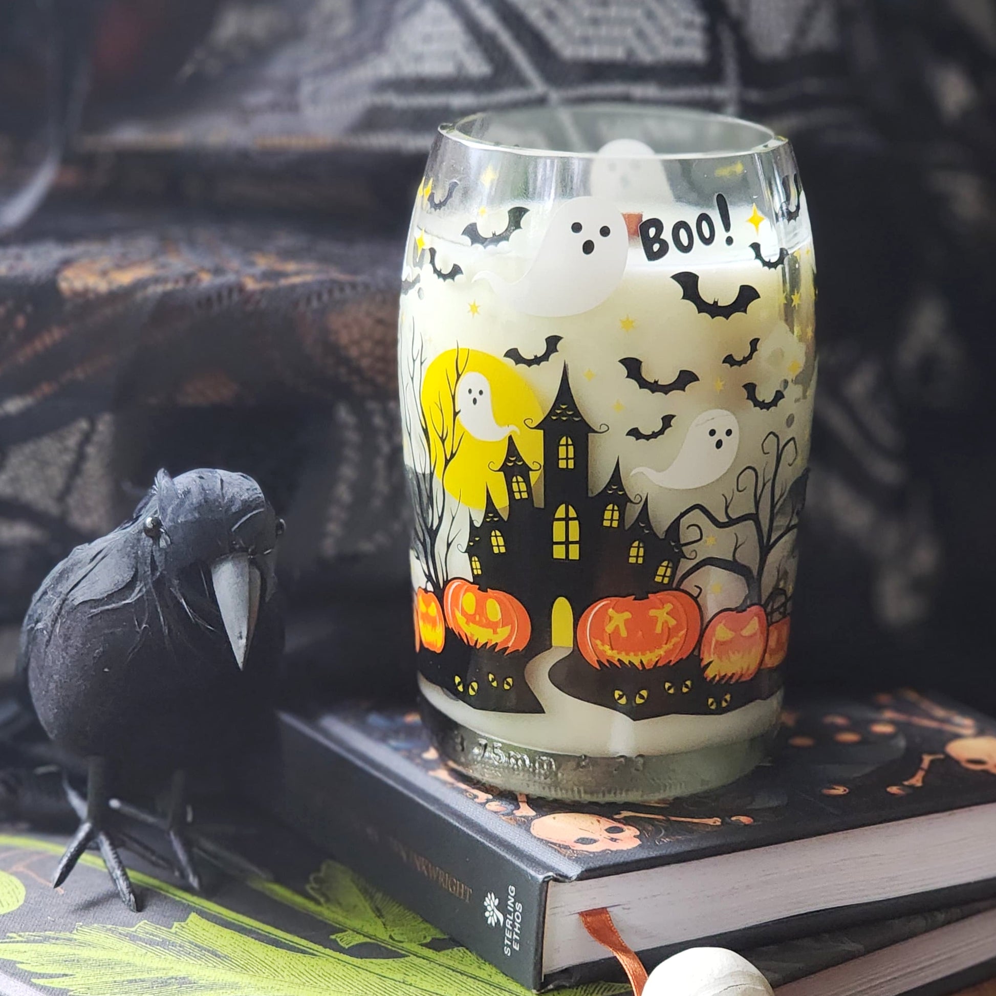 Halloween-themed wine bottle candle with ghost, pumpkin, and castle design on a book with a black crow.