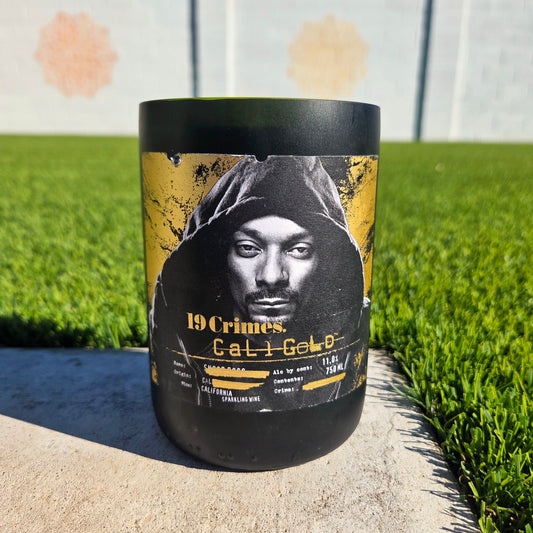 Black and gold wine bottle candle with a hooded Snoop on grass