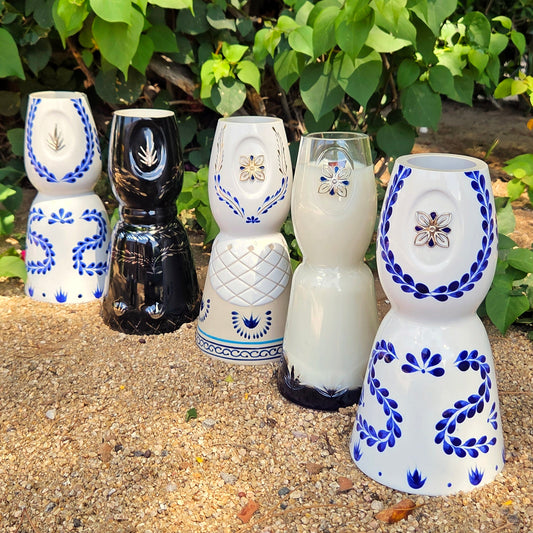 5 Clase Azul bottles that have been cut and made into candles.  sitting outside in front of green bushes.