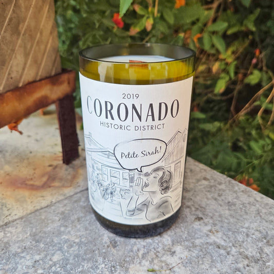 Wine Bottle Candle with art of the Coronado Historic District.  Sitting outdoors on a stone surface in front of green bushes.