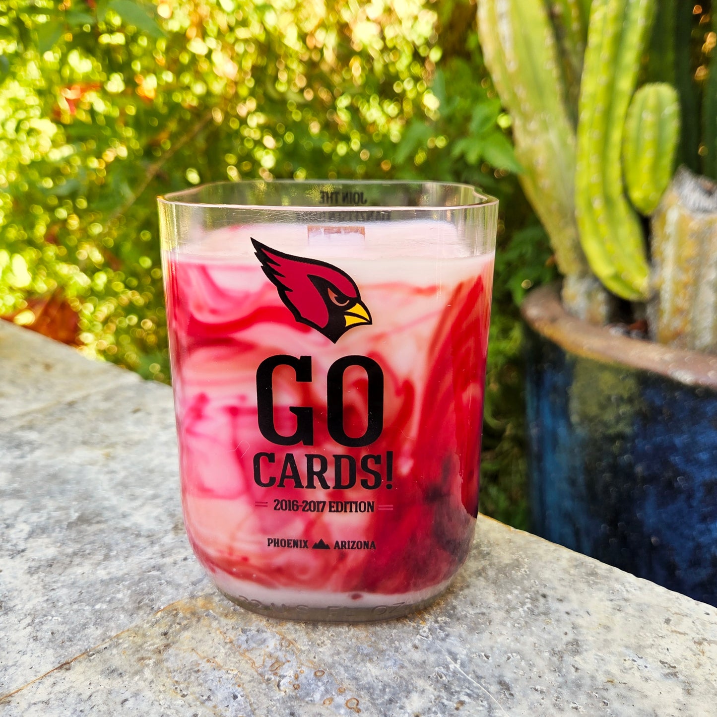 recyced milk bottle candle with red and white wax and 'GO CARDS!' text on a stone surface with cacti in the background