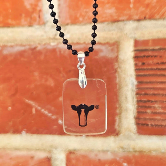 Necklace with a clear pendant featuring a black dairy cow logo against a brick wall background