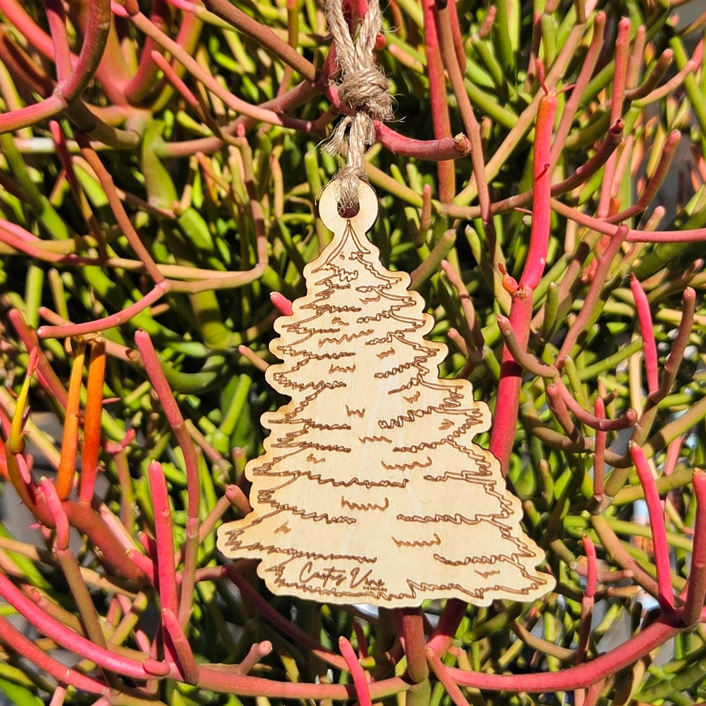 Wooden pine tree air freshener hanging on pink and green desert foliage