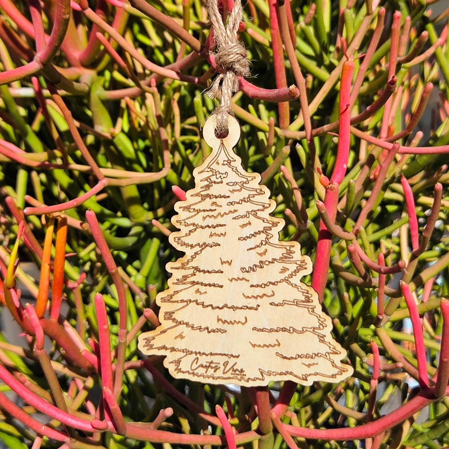 Wooden pine tree air freshener hanging on pink and green desert foliage