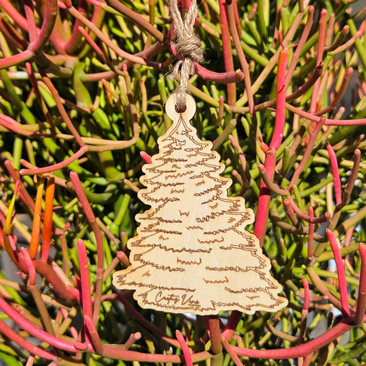 Wooden pine tree air freshener hanging on pink and green desert foliage