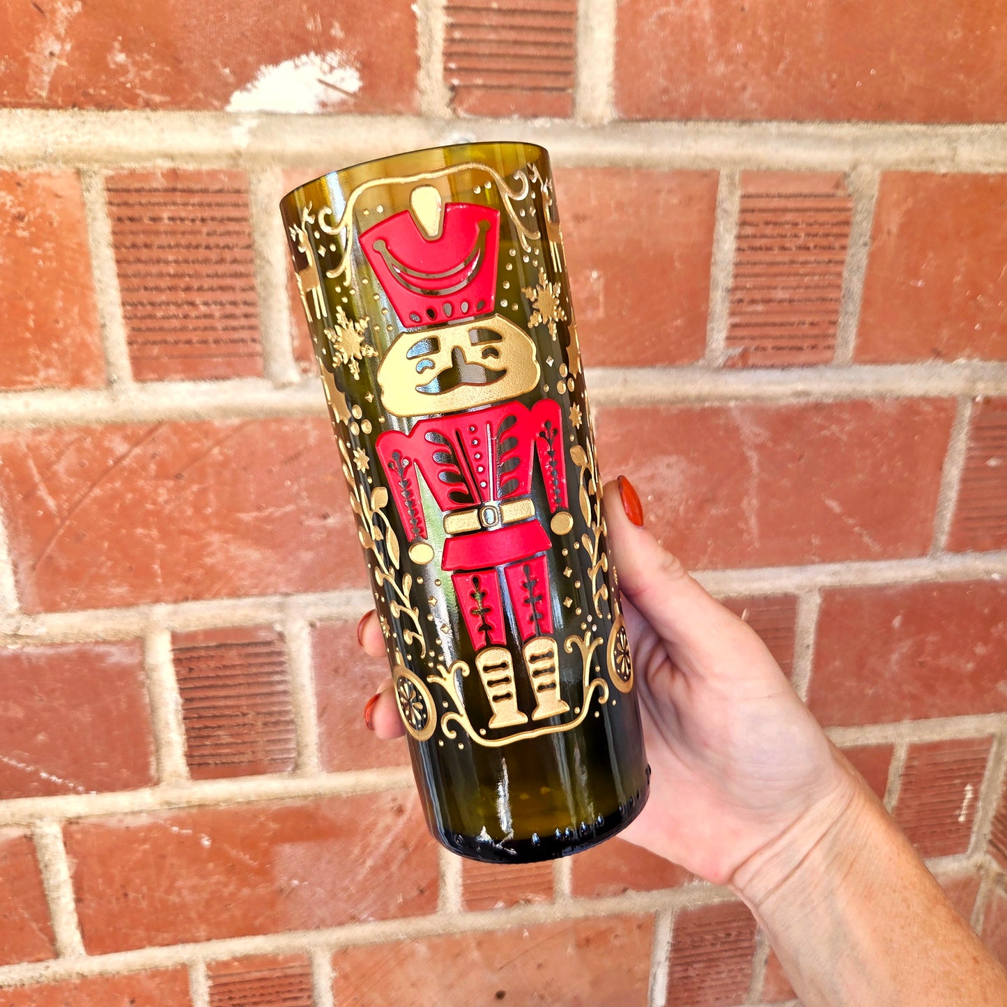 Etched red/gold nutcracker wine bottle candle held against a brick wall