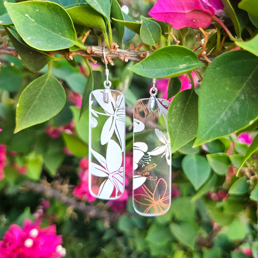 Reclaimed glass from wine bottles made into earring with a delicate white and pink floral design.  Hanging outdoors on a lush bush.