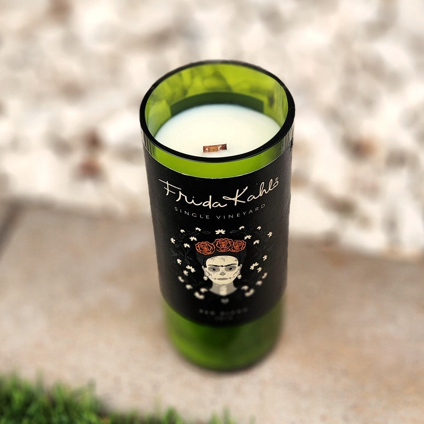 Angled look inside a Frida Kahlo wine bottle candle with white coconut soy wax and a wooden wick, housed in a deep green upcycled glass container with a striking black and floral label.

