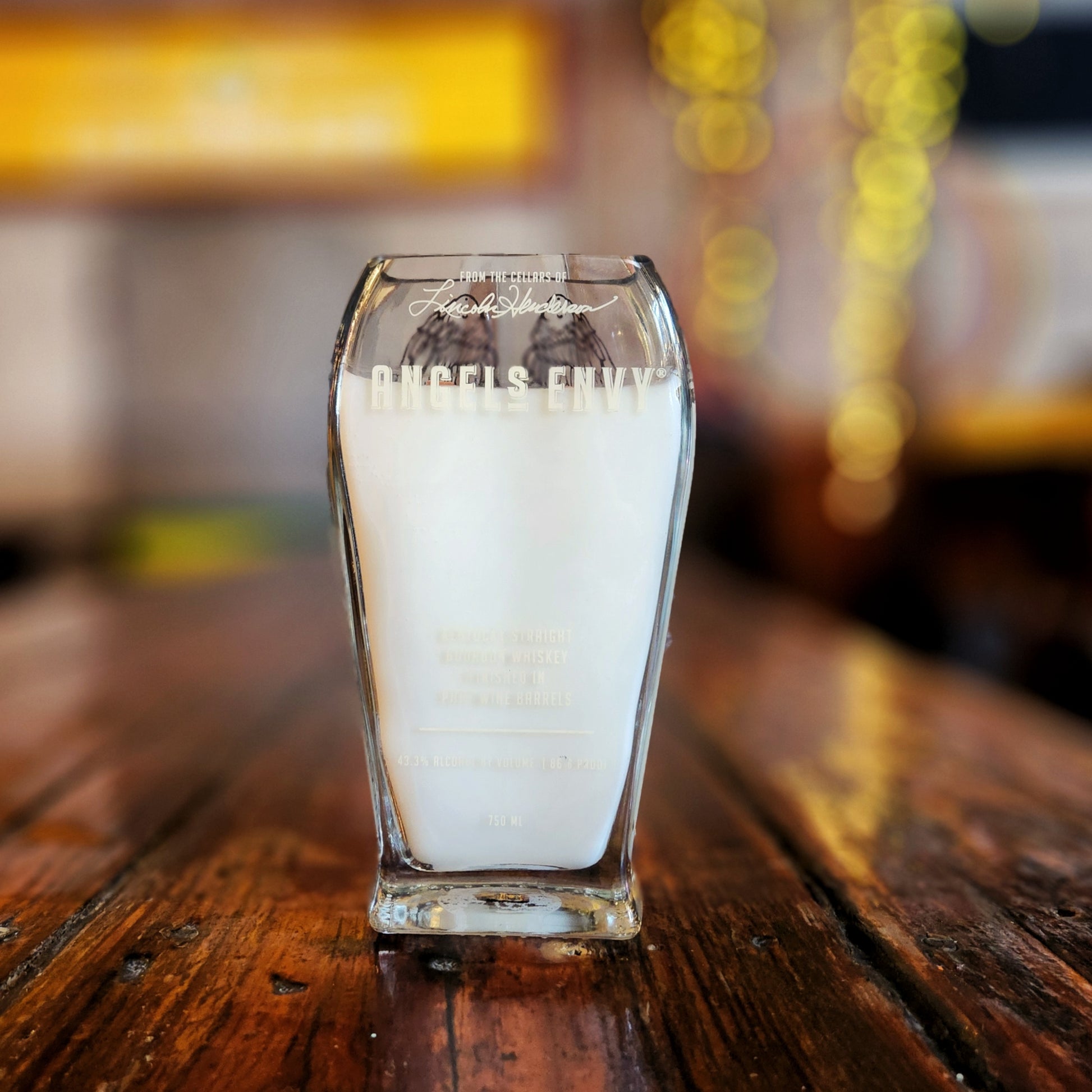 Front-facing image of a luxury recycled liquor bottle candle featuring the Angel’s Envy etched label, filled with creamy coconut soy wax and styled with a sustainable wooden wick.

