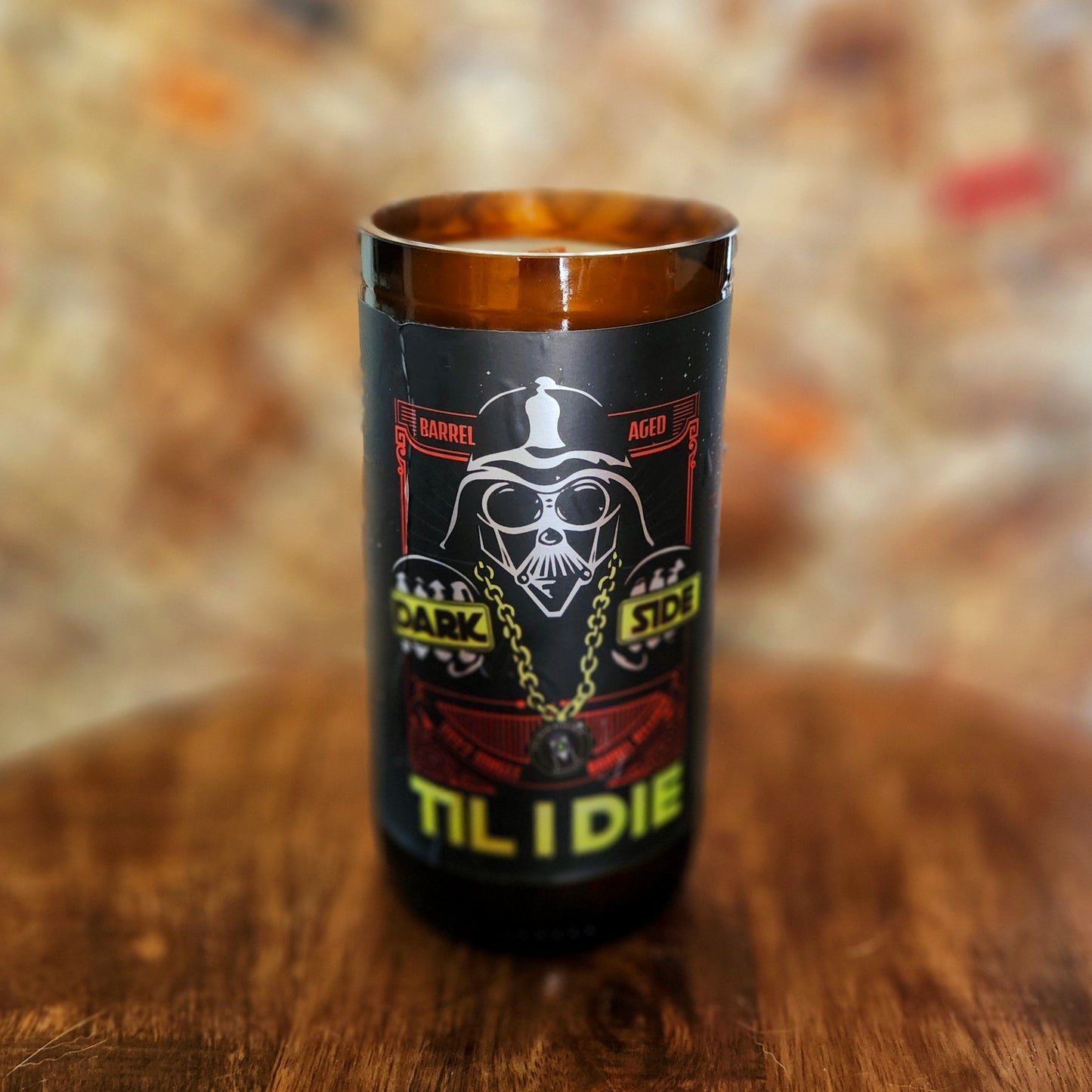 Hand-poured coconut soy candle in a recycled brown beer bottle featuring a bold graphic of a helmeted figure in sunglasses with gold chains, surrounded by text reading “Dark Side Til I Die.” Eco-friendly and non-toxic with a wooden wick.